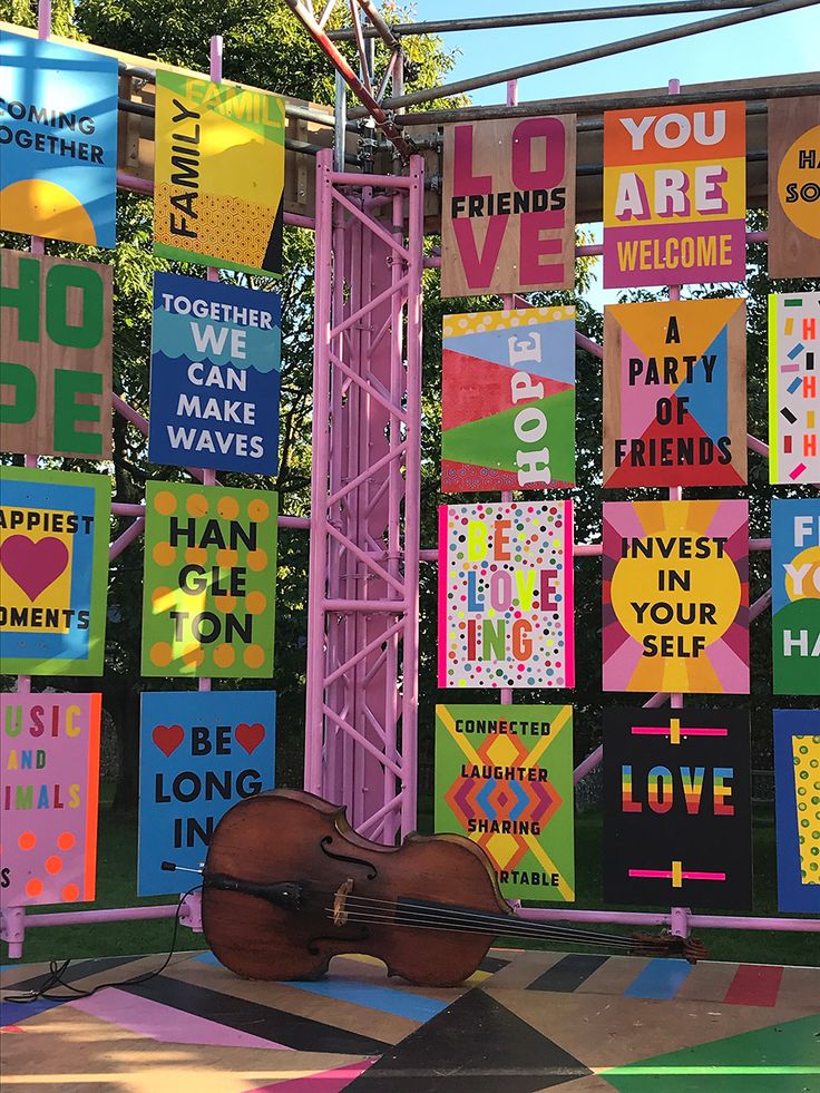 a violin sitting on the ground in front of some colorful signs and banners that say, you are welcome