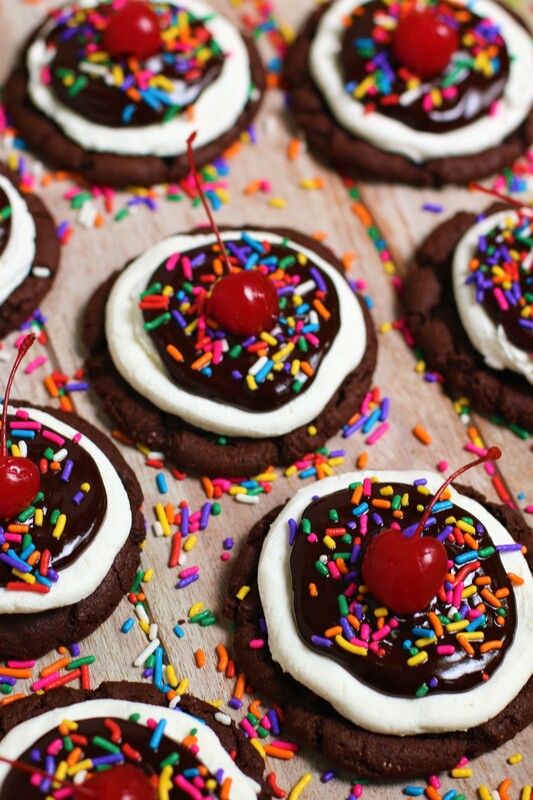 chocolate cookies with white frosting, sprinkles and cherries on top