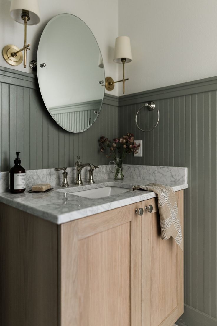 a bathroom vanity with two sinks and a large round mirror above it, in front of green paneled walls