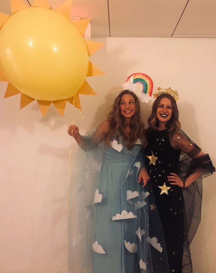 two women standing next to each other in front of a wall with balloons and stars on it