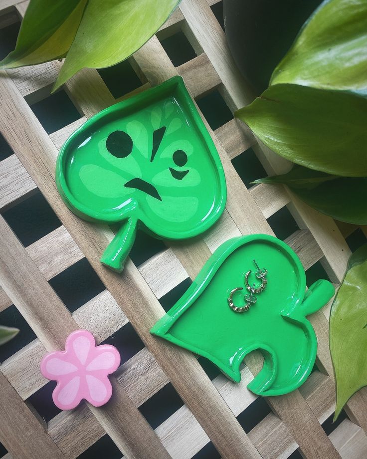 two green plates with faces on them sitting next to some leaves and flowers in the background