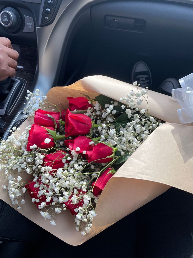 a bouquet of red roses and baby's breath sits in the driver's seat of a car