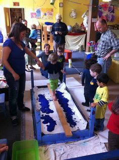 a group of people standing around a table with blue cake on it and children in the background