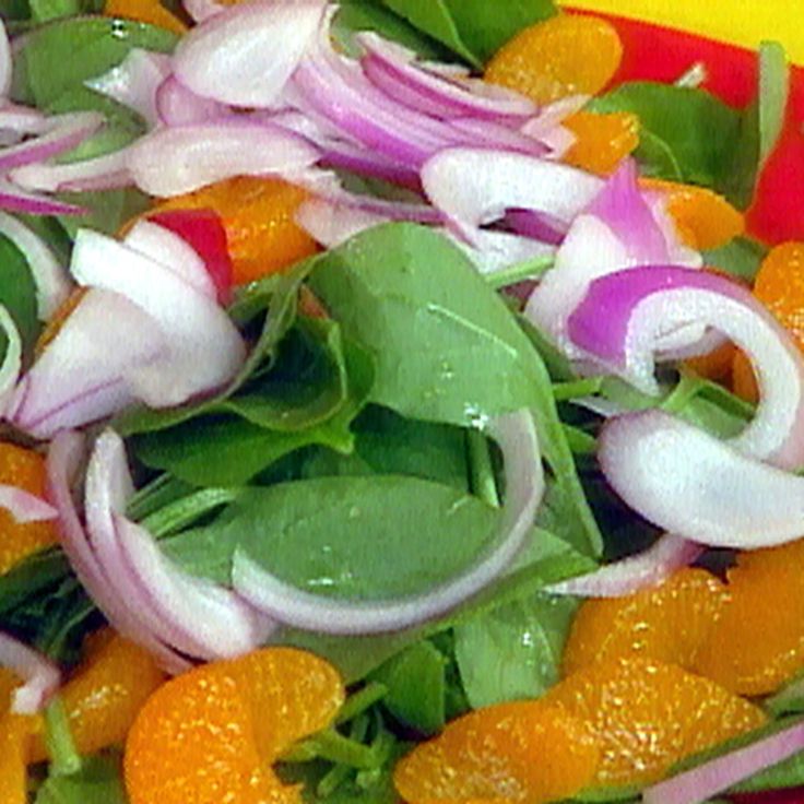 a salad with onions, oranges and spinach on a red plate in front of a yellow background