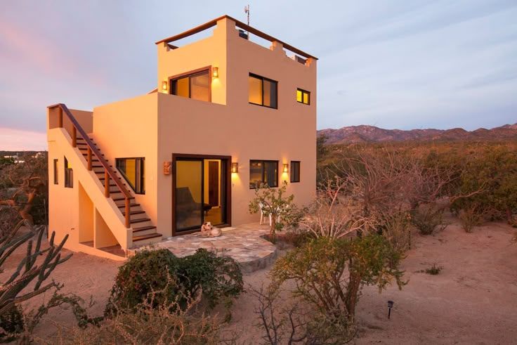 a house with stairs leading up to it in the middle of desert landscape at dusk