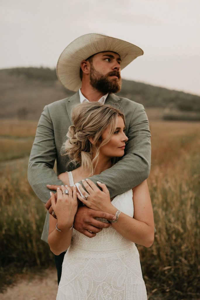 a man in a cowboy hat hugging a woman wearing a white wedding dress and ring