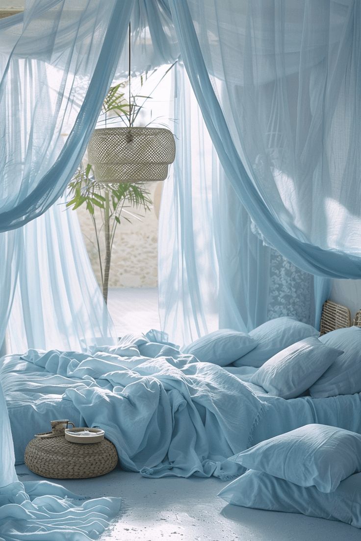 a bed covered in blue sheets and pillows next to a window with curtains on it