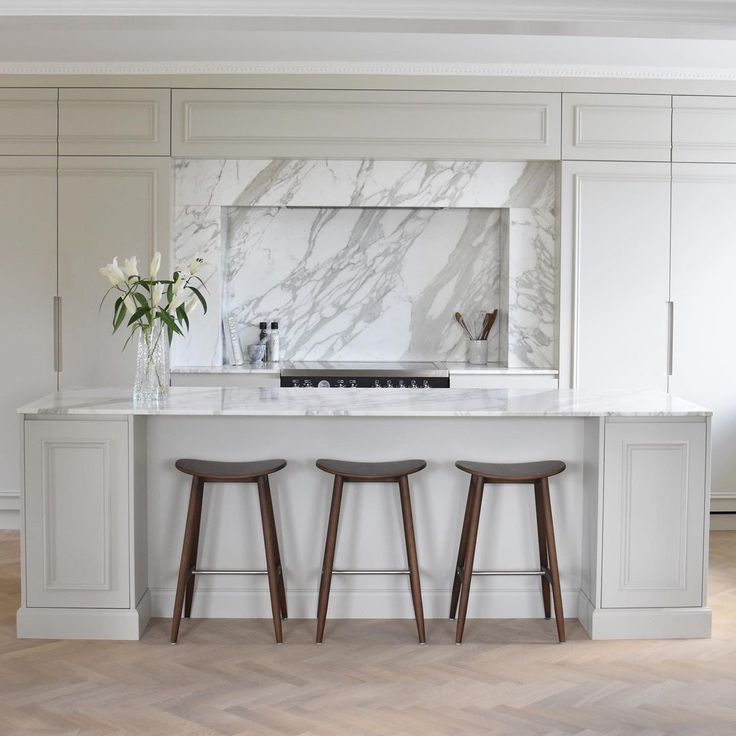 three stools are sitting in front of the kitchen island with marble backsplash