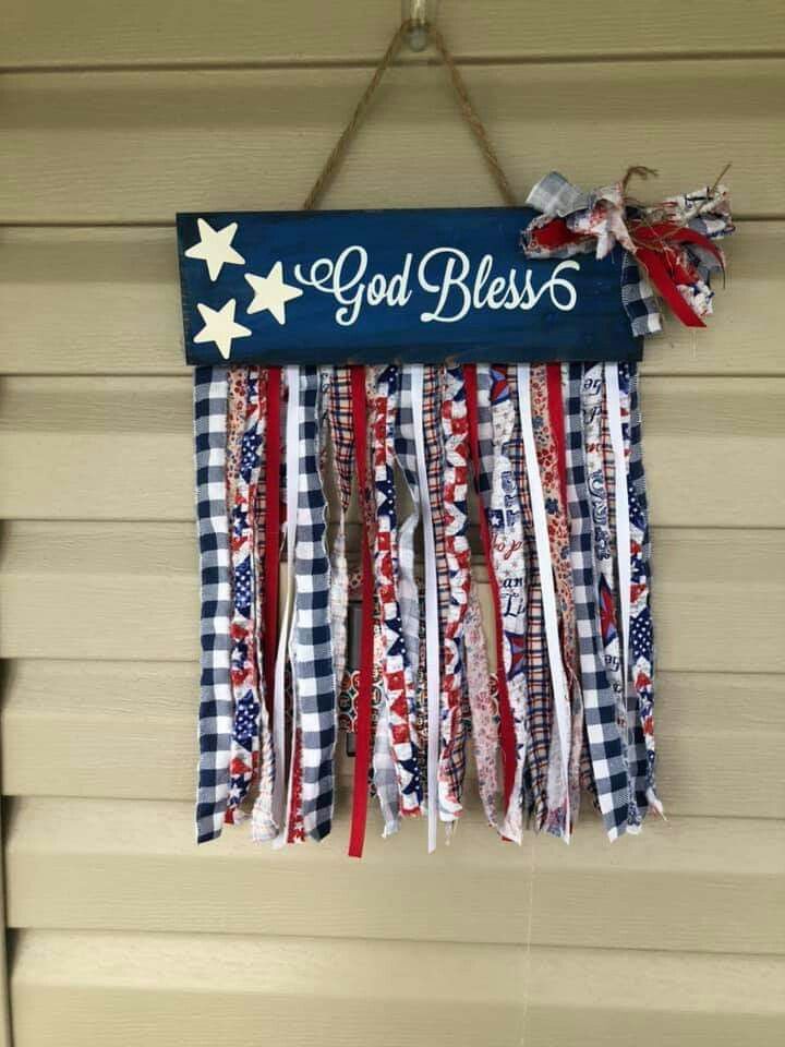 a patriotic sign hanging from the side of a house with ribbons attached to it's sides