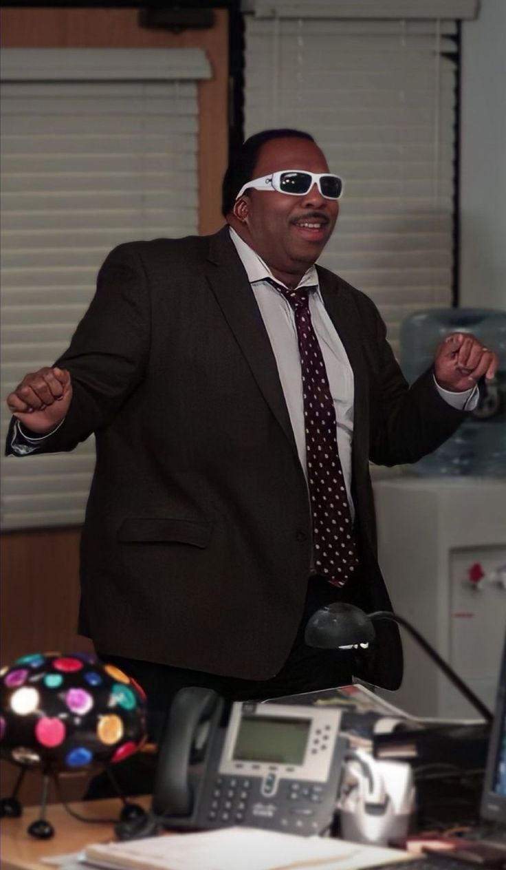 a man in a suit and tie with sunglasses on his face standing next to a desk