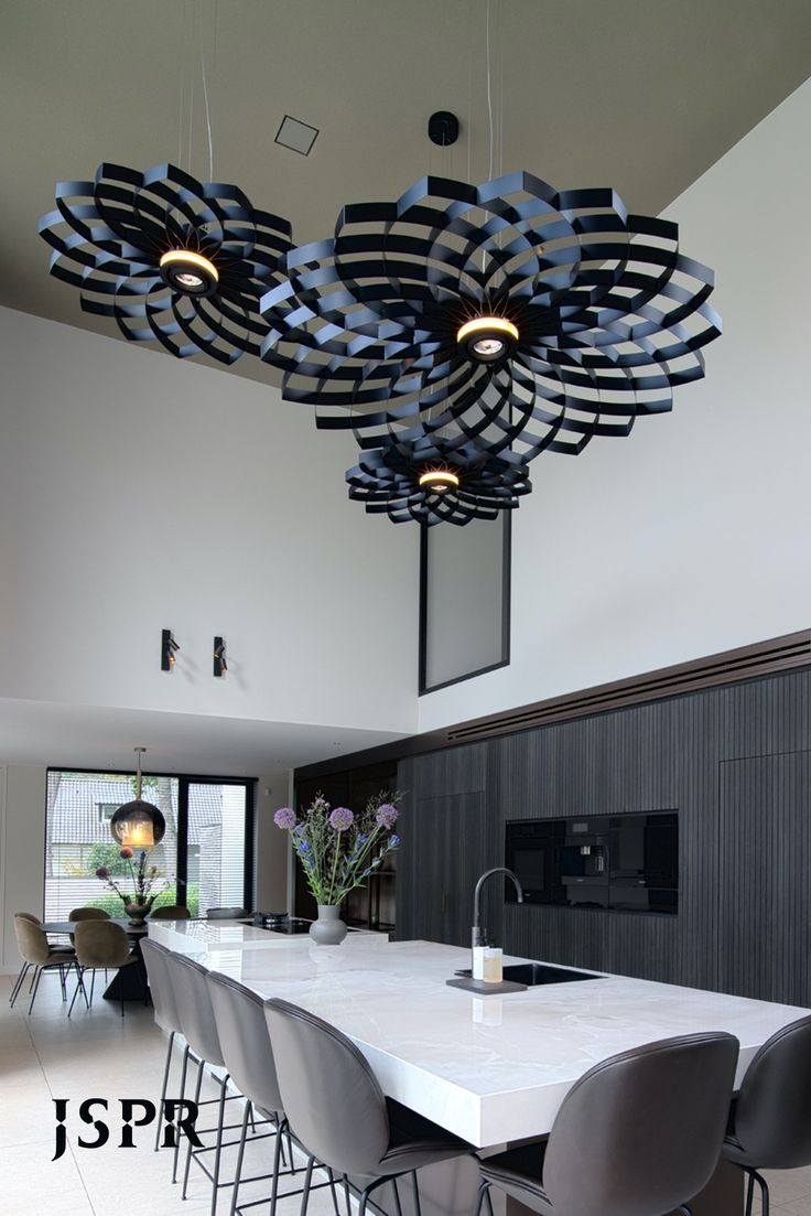 a large white table surrounded by grey chairs and black lights hanging from the ceiling above it