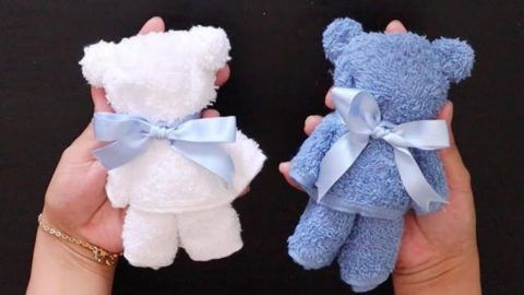 two small teddy bears are being held by someone's hands with blue bows on them