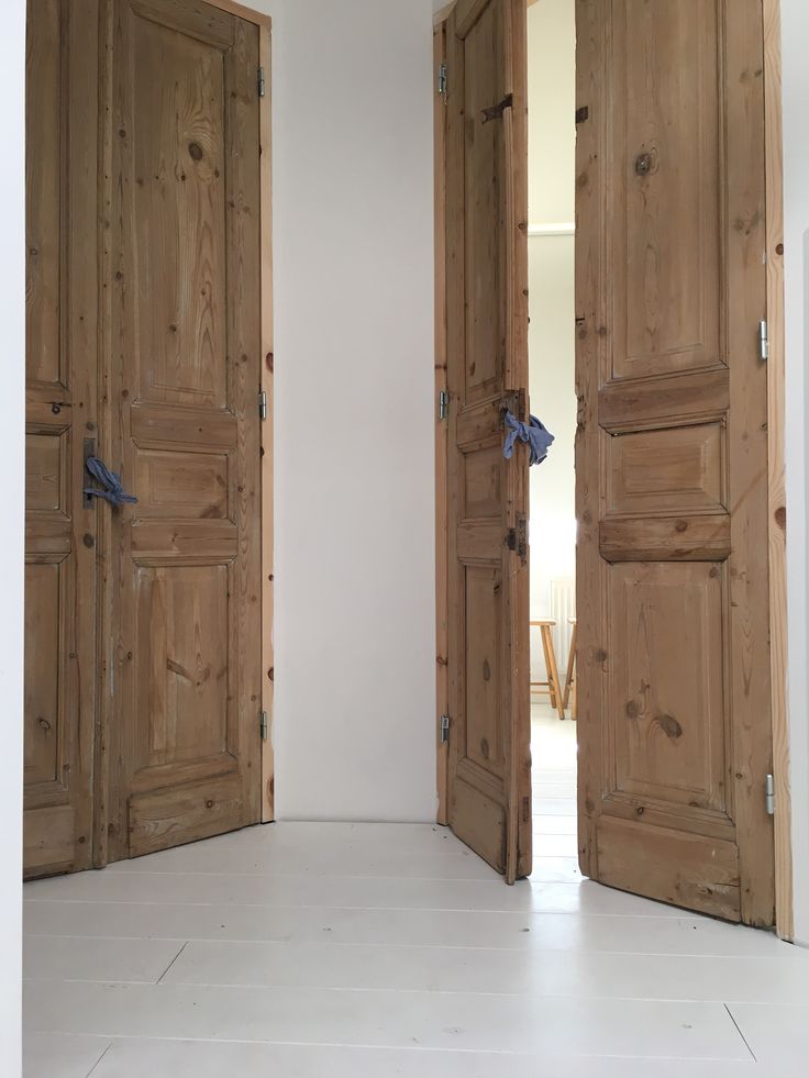 two open wooden doors in a room with white walls and floor tiles on the ground