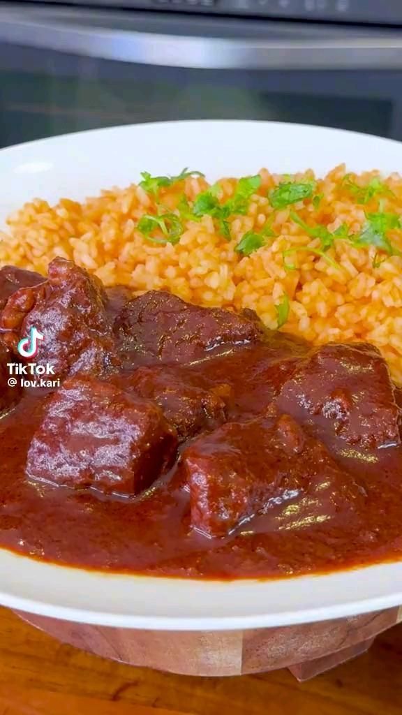 a white plate topped with meat and rice next to a fork on a wooden table