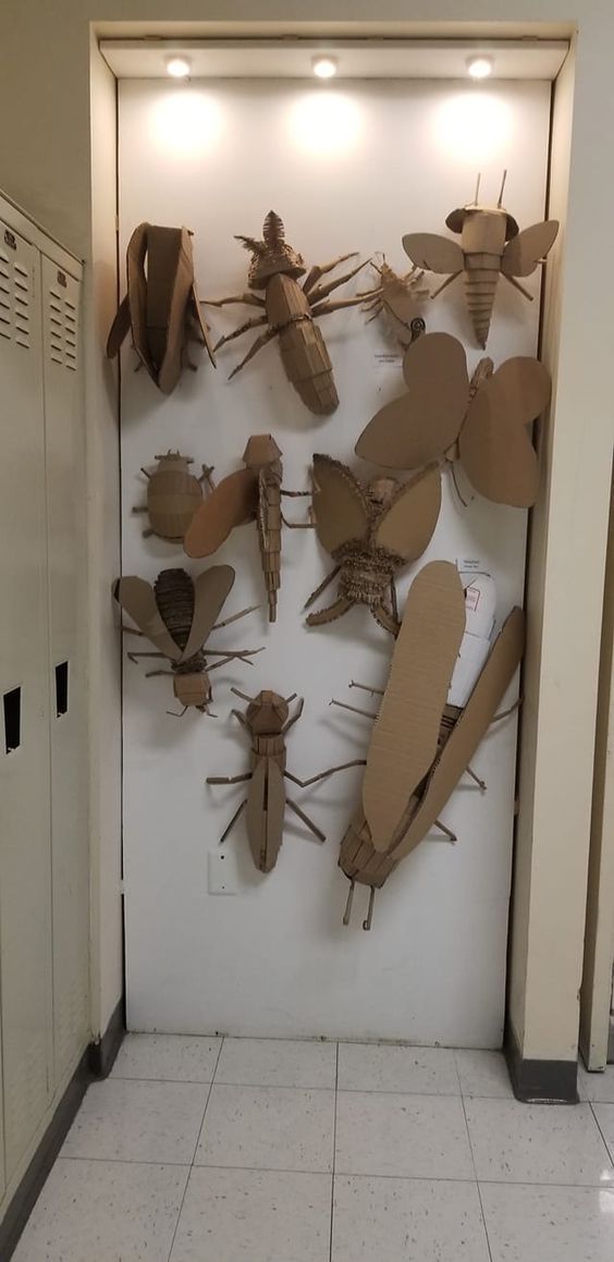 a group of cardboard insects mounted to the side of a wall in a hallway next to lockers