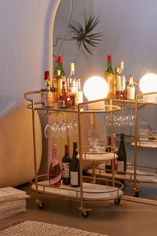 a gold bar cart with wine glasses and bottles on it in front of a mirror