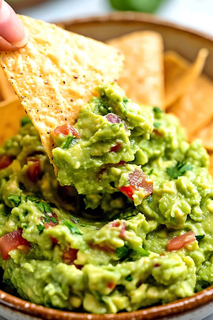 a person dipping guacamole into a bowl with tortilla chips