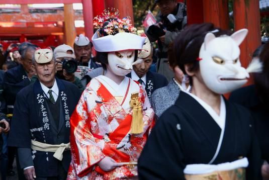 people in costumes walking down the street with masks on their faces and one person wearing a cat mask