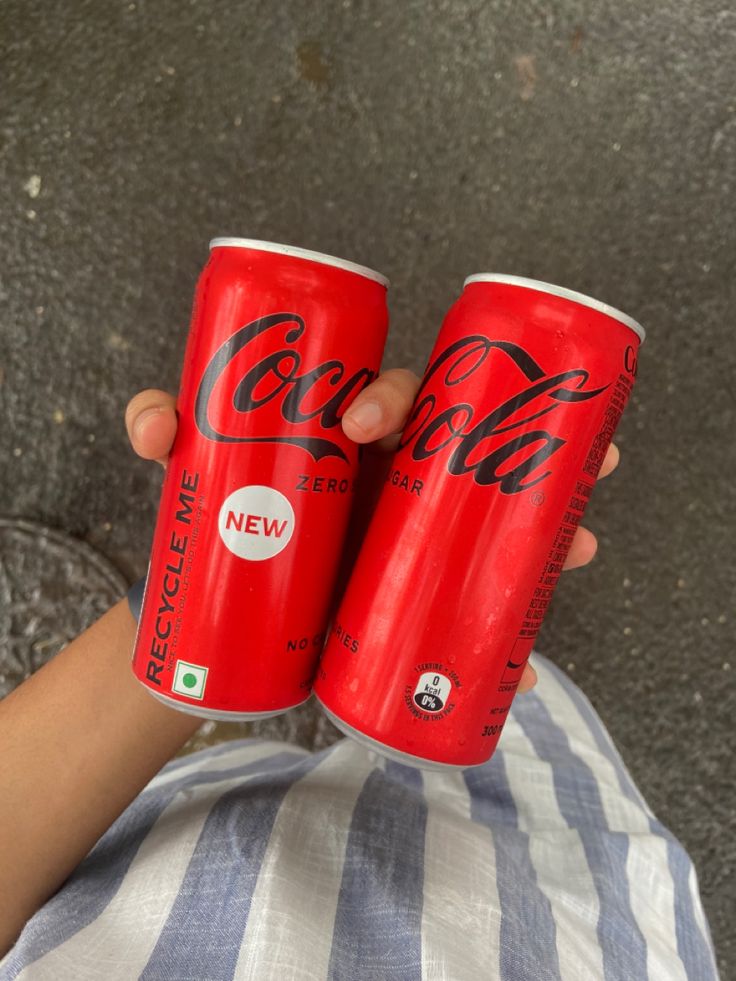 two cans of coca cola sitting on top of a person's lap next to each other