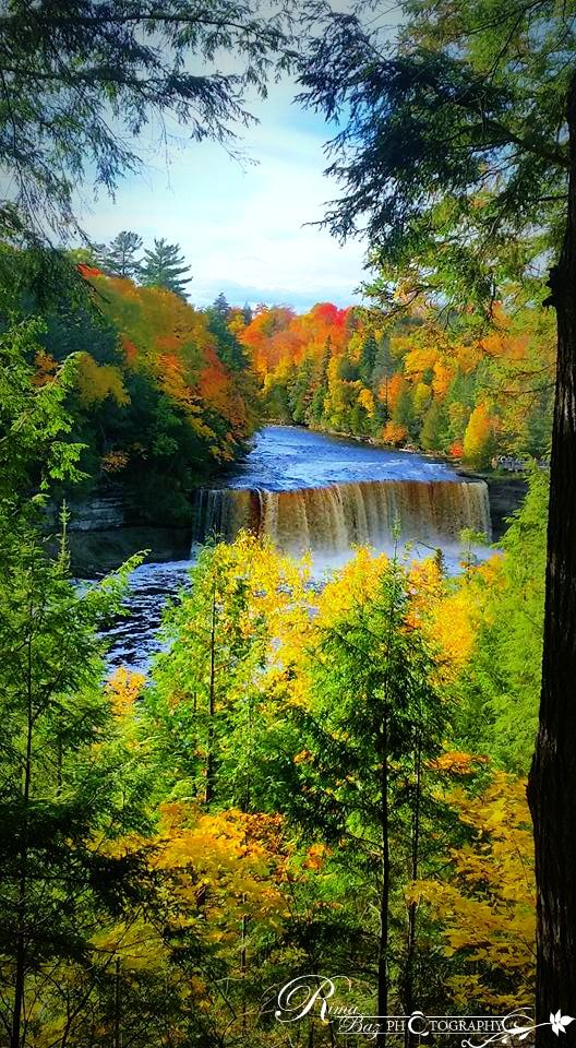 a waterfall surrounded by trees in the fall season with colorful leaves on it's sides