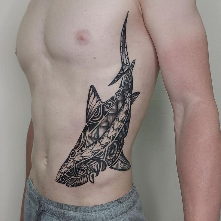 a man with a shark tattoo on his chest is standing in front of a white wall