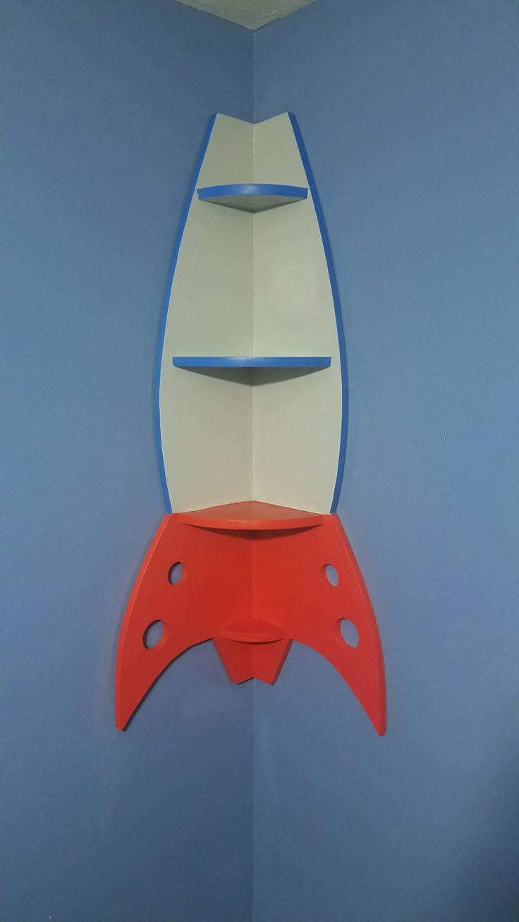 a red and white rocket ship hanging from the side of a wall in a blue room