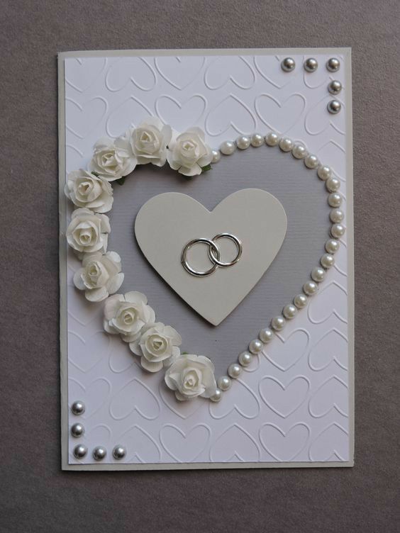 a heart shaped card with two wedding rings in the middle and white roses around it