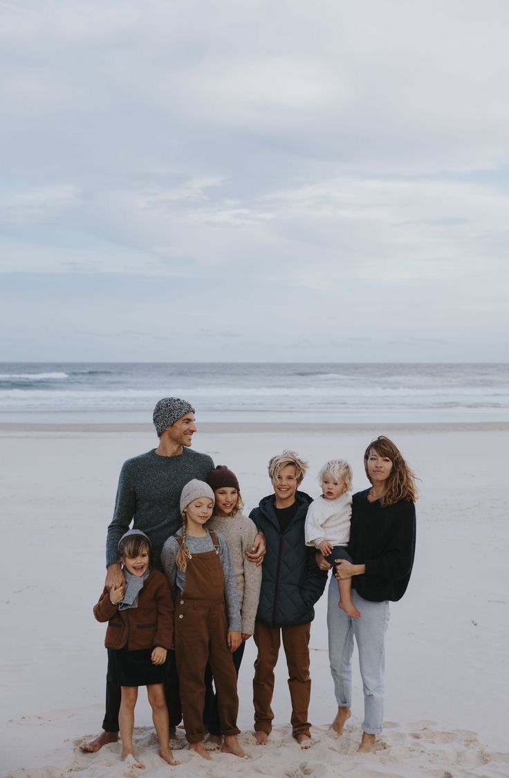 a group of people standing on top of a beach next to the ocean in winter