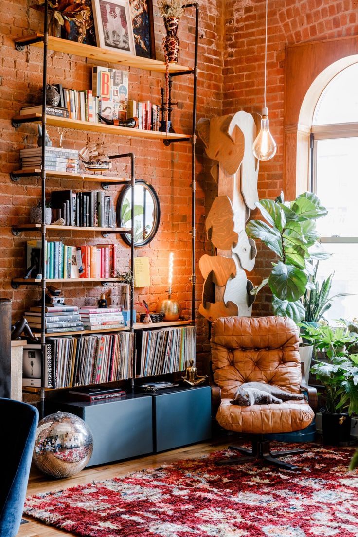 a living room filled with furniture and a large window covered in bookshelves next to a brick wall