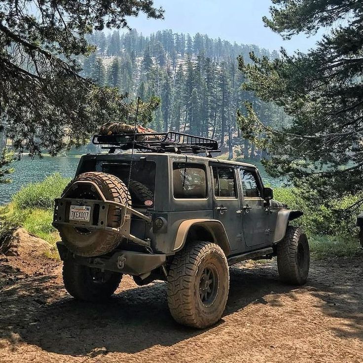 a jeep is parked on the side of a dirt road with trees in the background