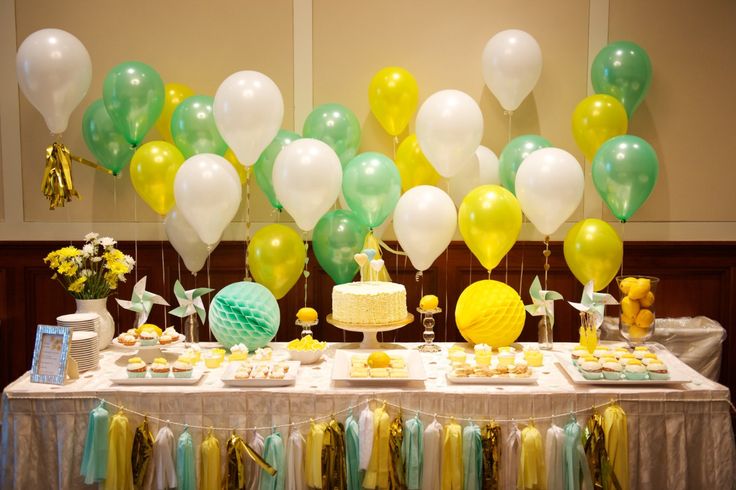 a table topped with lots of yellow and green balloons next to a cake covered in white frosting