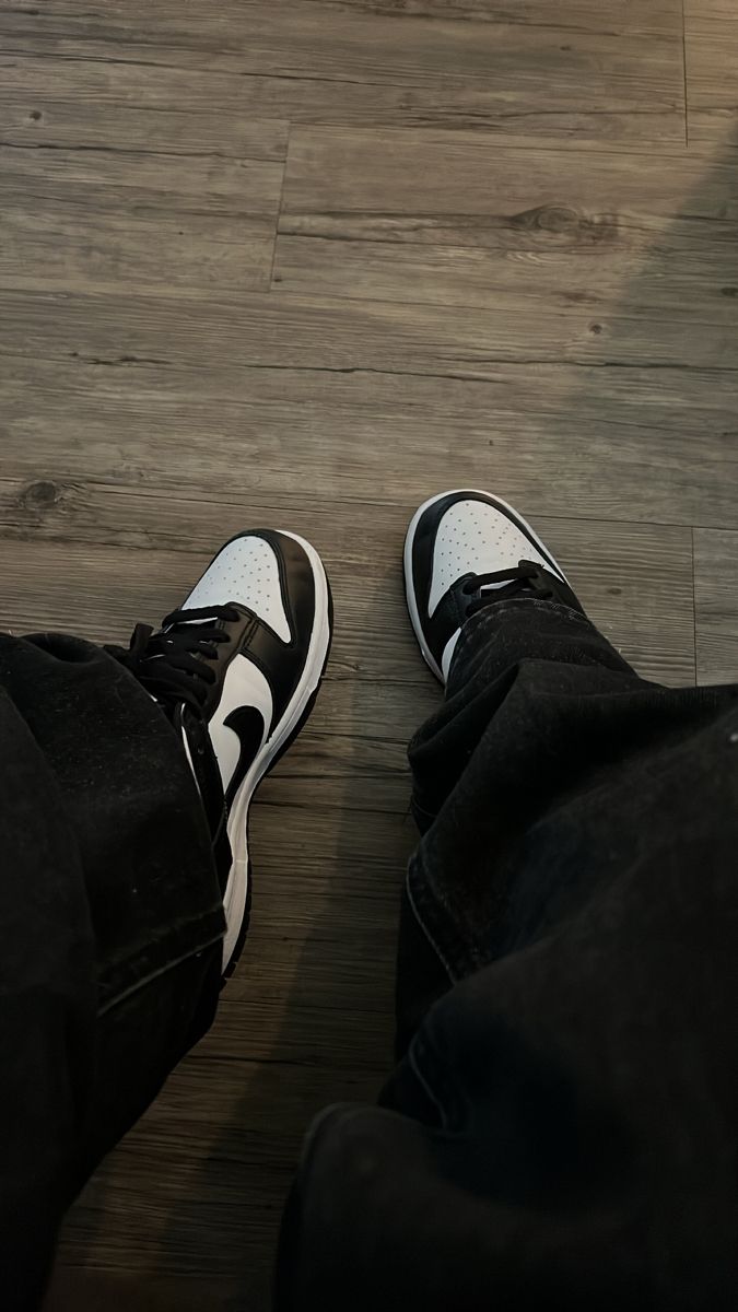 a pair of black and white shoes sitting on top of a wooden floor next to a person's legs