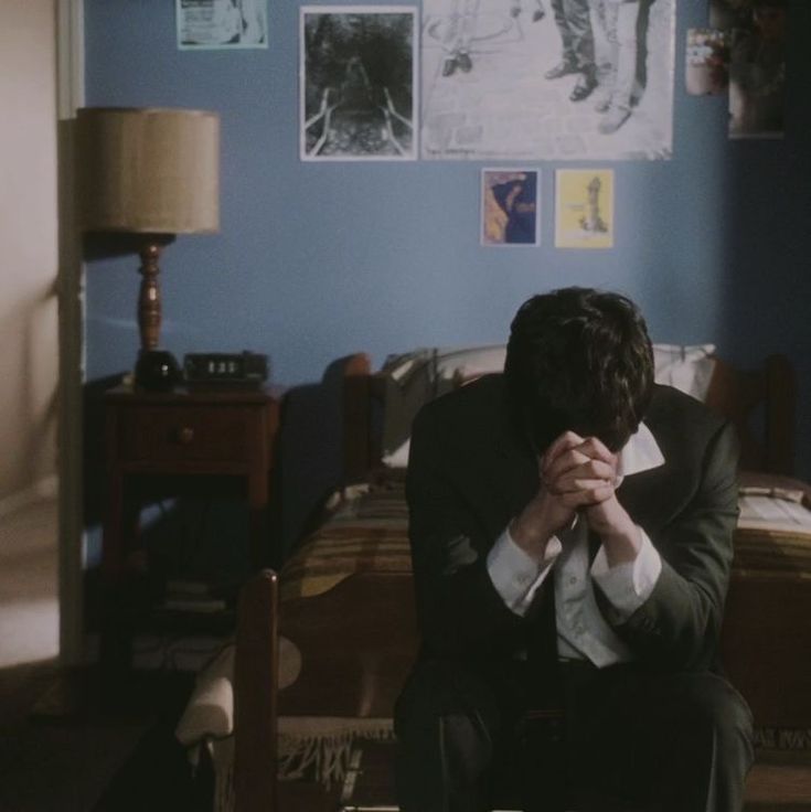 a man in a suit and tie sitting on a chair with his hands clasped to his face