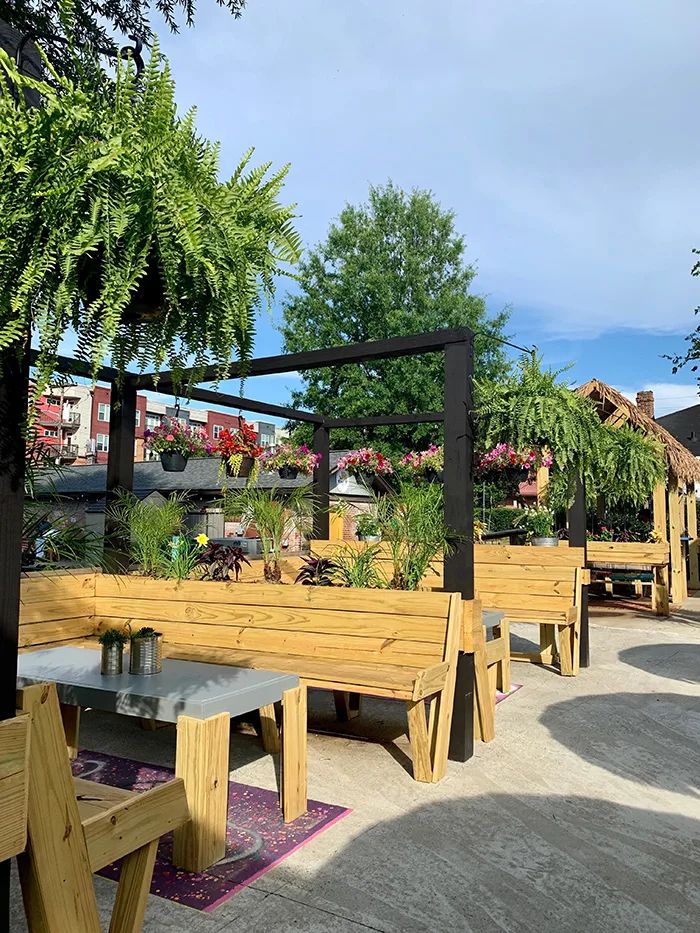 benches and tables are lined up in the shade on an outdoor patio with potted plants