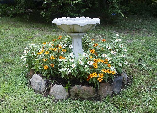 a bird bath sitting in the middle of a flower bed