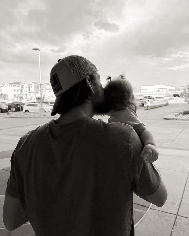 a man holding a baby in his arms while standing on the sidewalk next to a parking lot