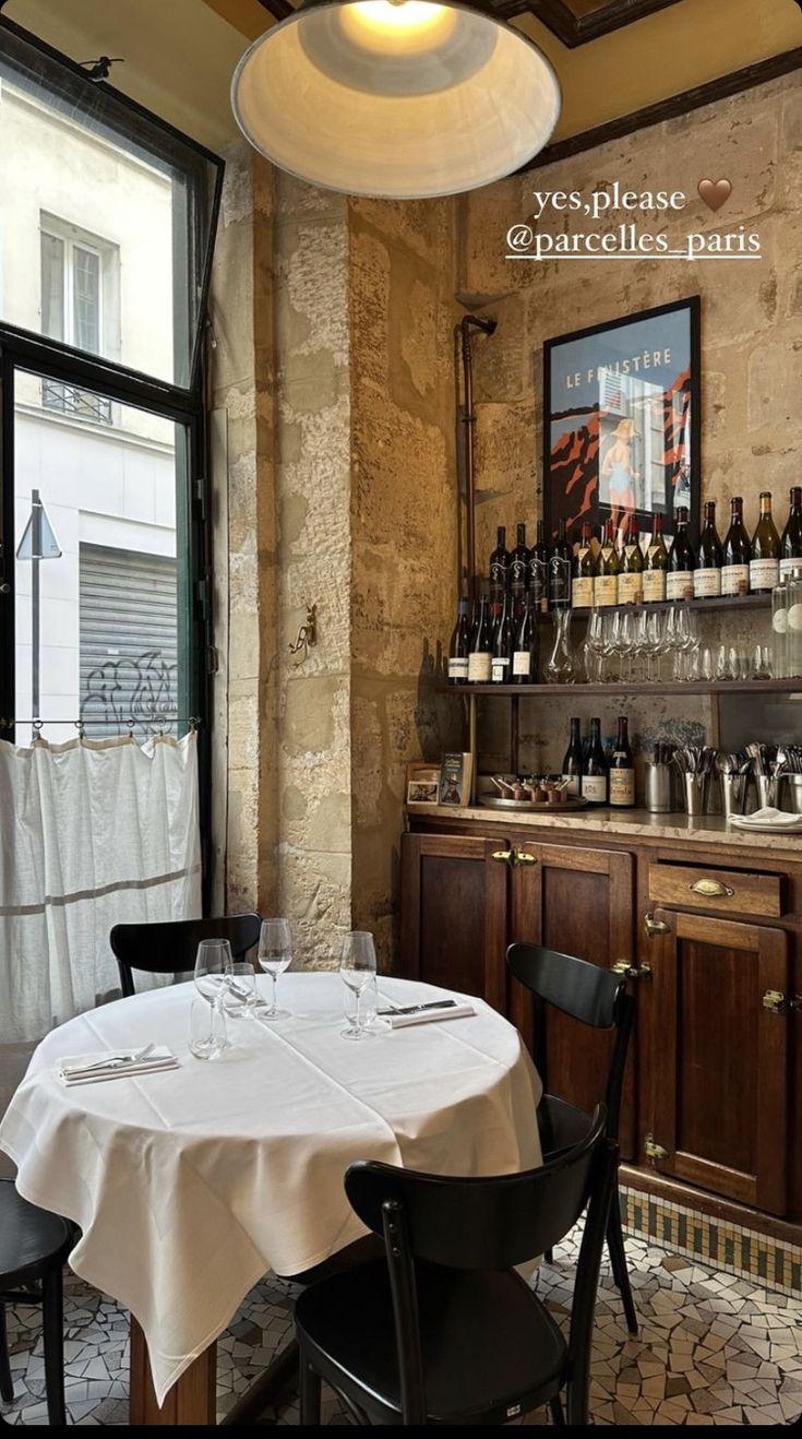 an empty table in a restaurant with wine bottles on the wall