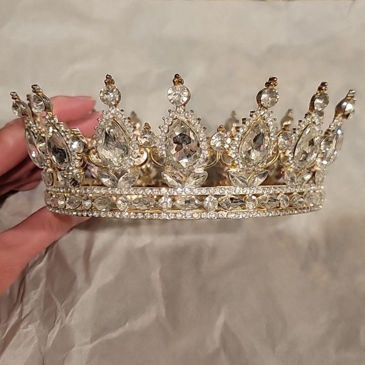 a hand holding a tiara on top of a white sheet