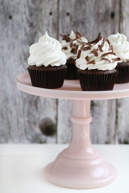 three cupcakes with white frosting and chocolate sprinkles on a pink cake plate