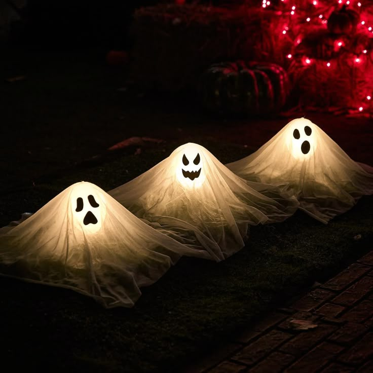 three lighted ghost decorations sitting on the ground in front of a tree with red lights