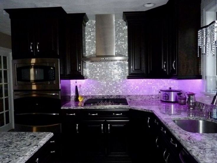 a kitchen with black cabinets and purple lights on the backsplash is pictured in this image