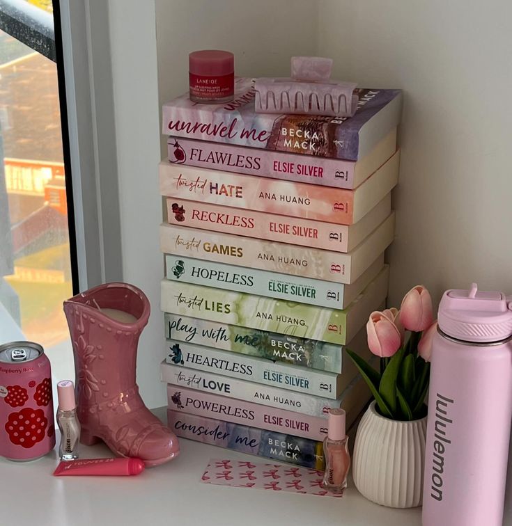 a stack of books sitting on top of a window sill next to a pink cup