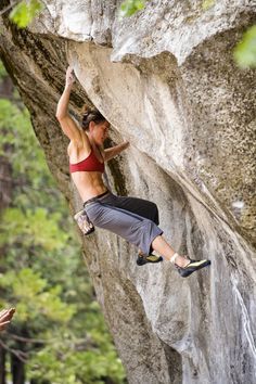 a woman climbing up the side of a large rock with her hands on her hips