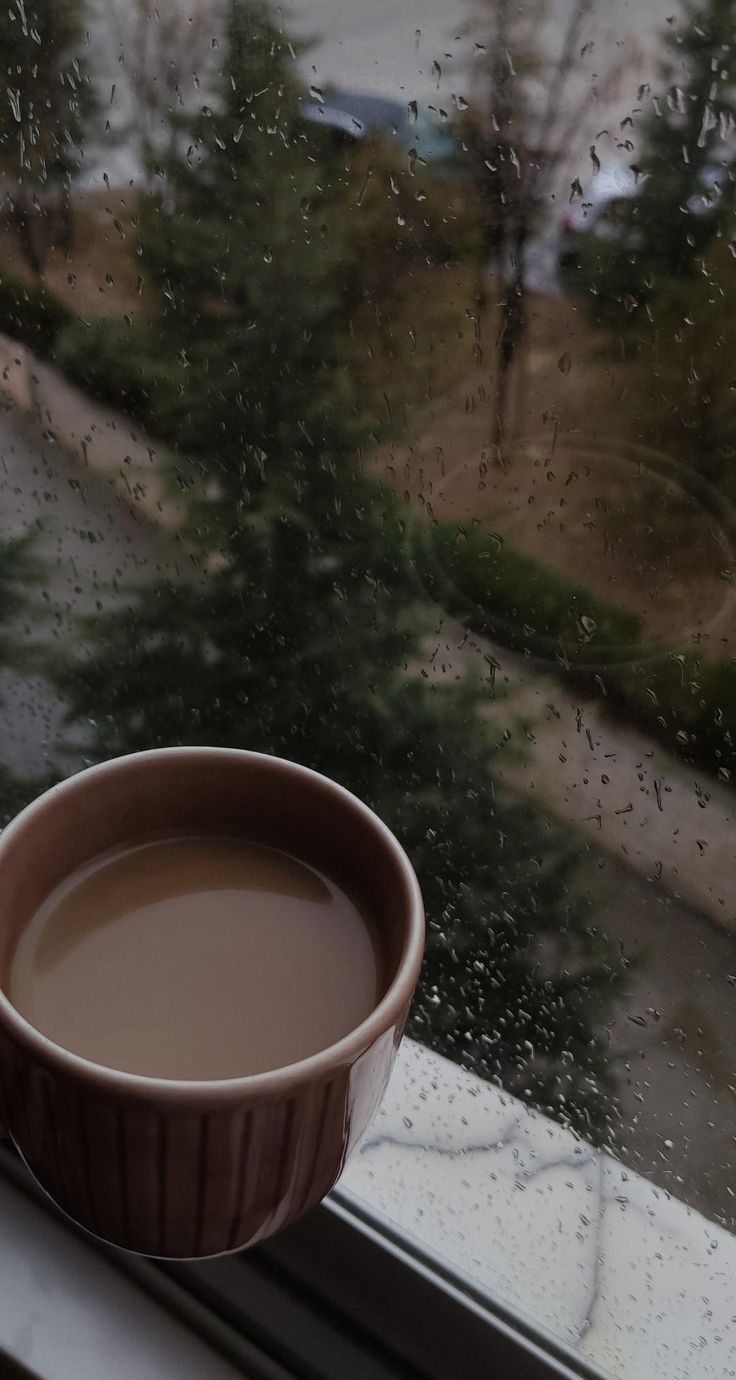 a cup of coffee sitting on top of a window sill next to a tree