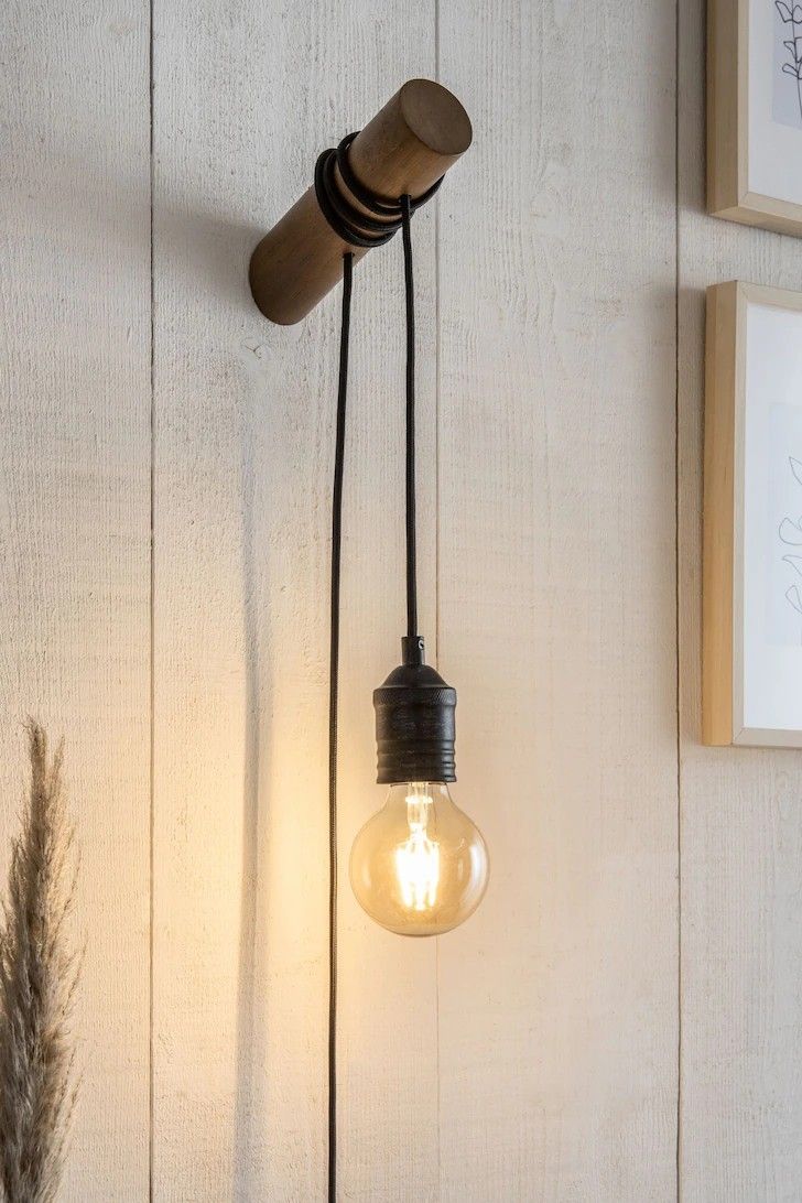 a light bulb hanging from the side of a white wall next to a vase with flowers