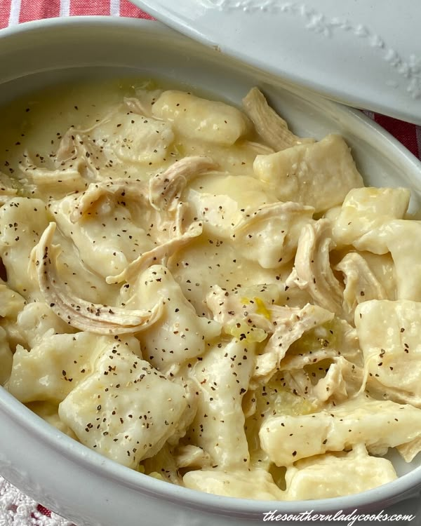 a white bowl filled with pasta and sauce on top of a red and white checkered table cloth