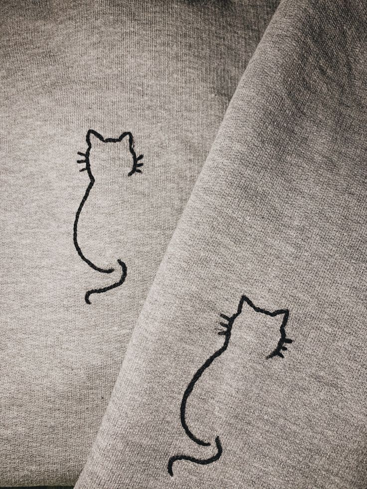 two gray sweaters with black cats drawn on the front and back of them, sitting next to each other