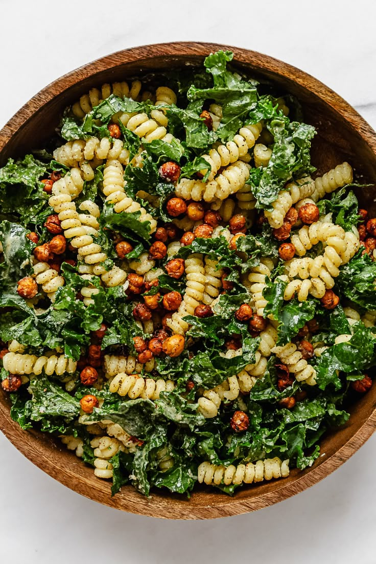 a wooden bowl filled with pasta and greens