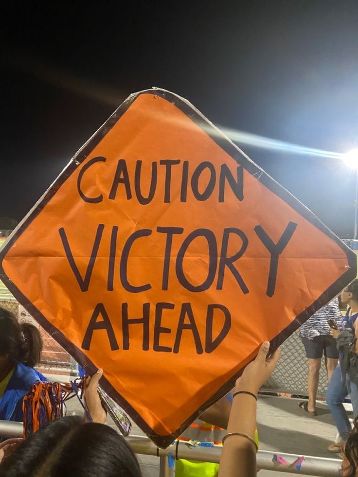 an orange caution sign with the words victory ahead written on it in front of a crowd