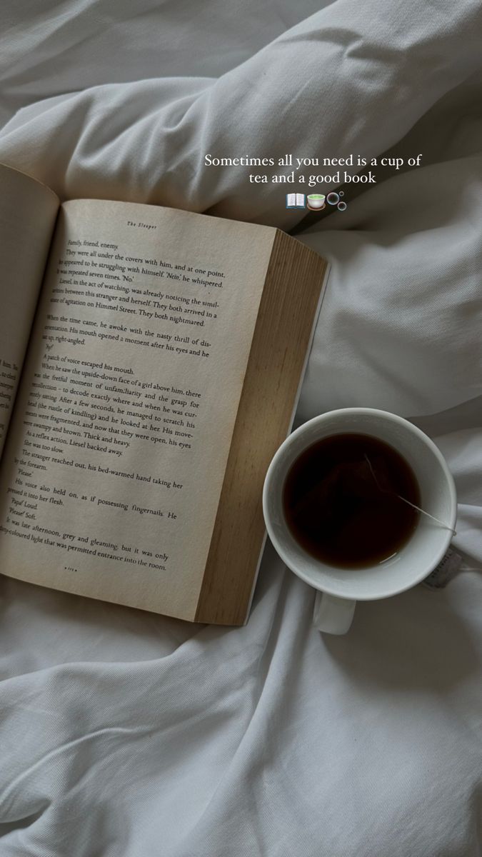 an open book sitting on top of a white bed next to a cup of coffee